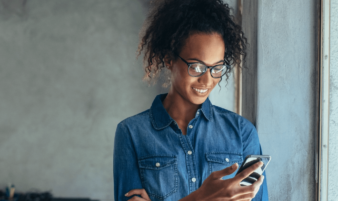 Woman looks down at mobile phone while smiling